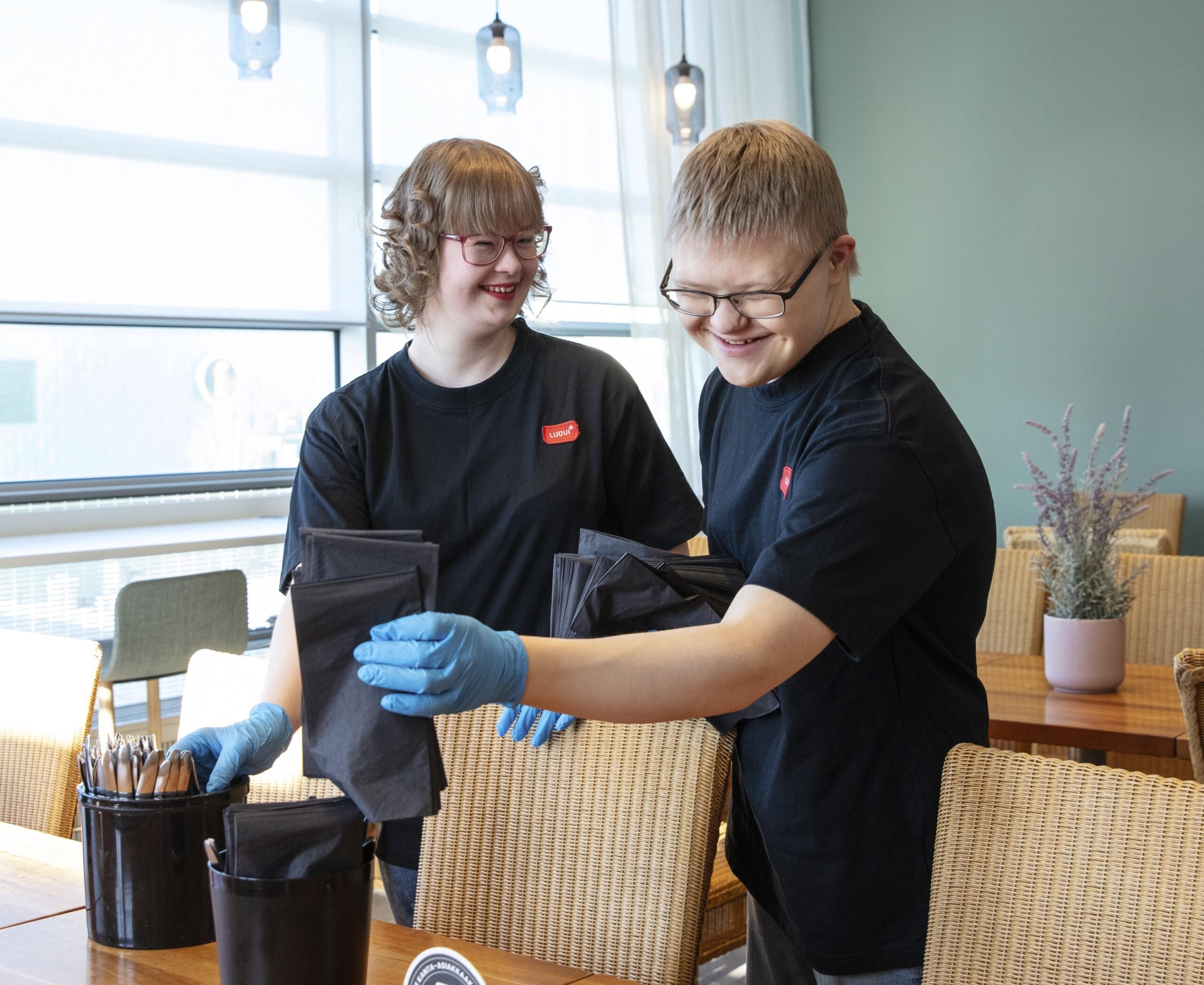 Kaksi TELMA-opiskelijaa ravintolassa asettelemassa astioita pöytään.