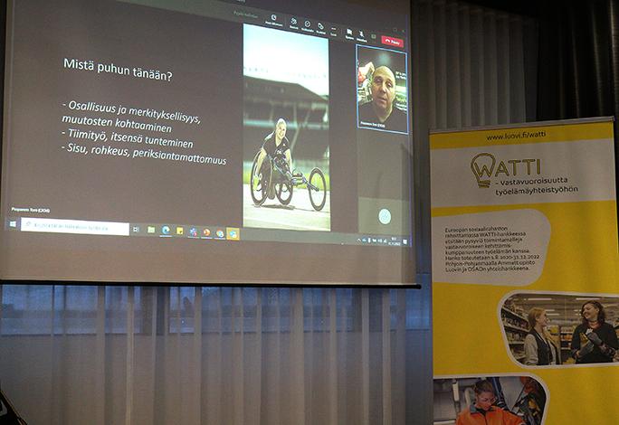 WATTI-hankkeen esittely roll up sekä valkokangas, jossa näkyy videopuhelunäyttö, jossa kuvassa Toni Piispanen sekä hänen esityksensä.