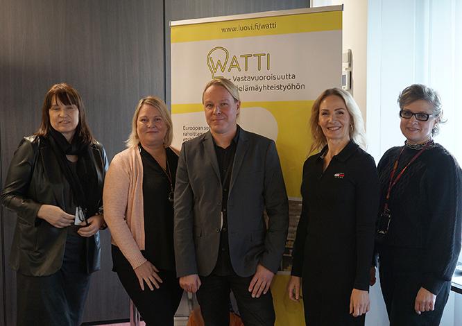 Merja Paloniemi, Sanna Määttä, Marko Ylisirkka, Sari Kauppila ja Sanna Syren seisovat vierekkäin ja katsovat kameraan WATTI-hankkeen esittely roll upin edessä.
