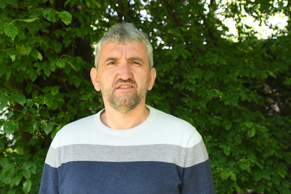 A photo of Silvo Vidergar with a blue-grey and white shirt and some greenery behind.