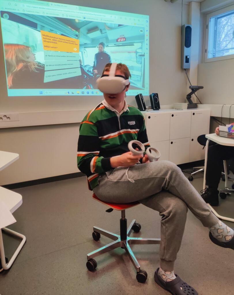 Opiskelija istuu tuolissa, päässään VR-lasit ja käsissään VR-ohjaimet.