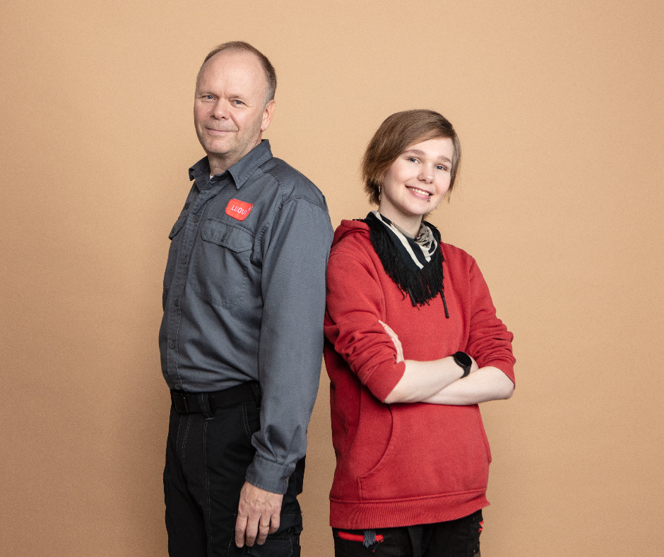 Luovin työntekijä ja opiskelija seisovat hymyillen selät vastakkain ja katsovat kameraan. Opiskelijalla on kädet puuskassa.