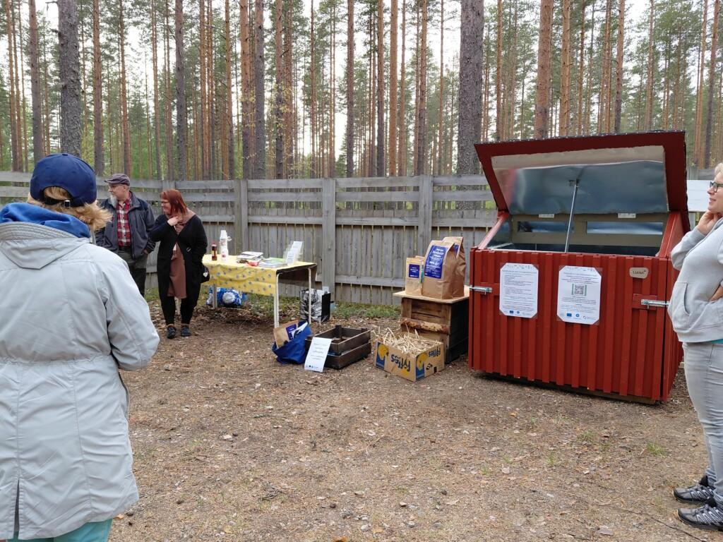 Ihmisiä kerääntyneenä pihalla olevan kompostin ympärille.