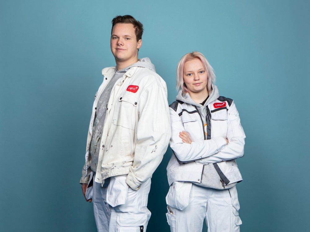 Kaksi opiskelijaa seisoo selät vastakkain ja katsoo kameraan hymyillen.