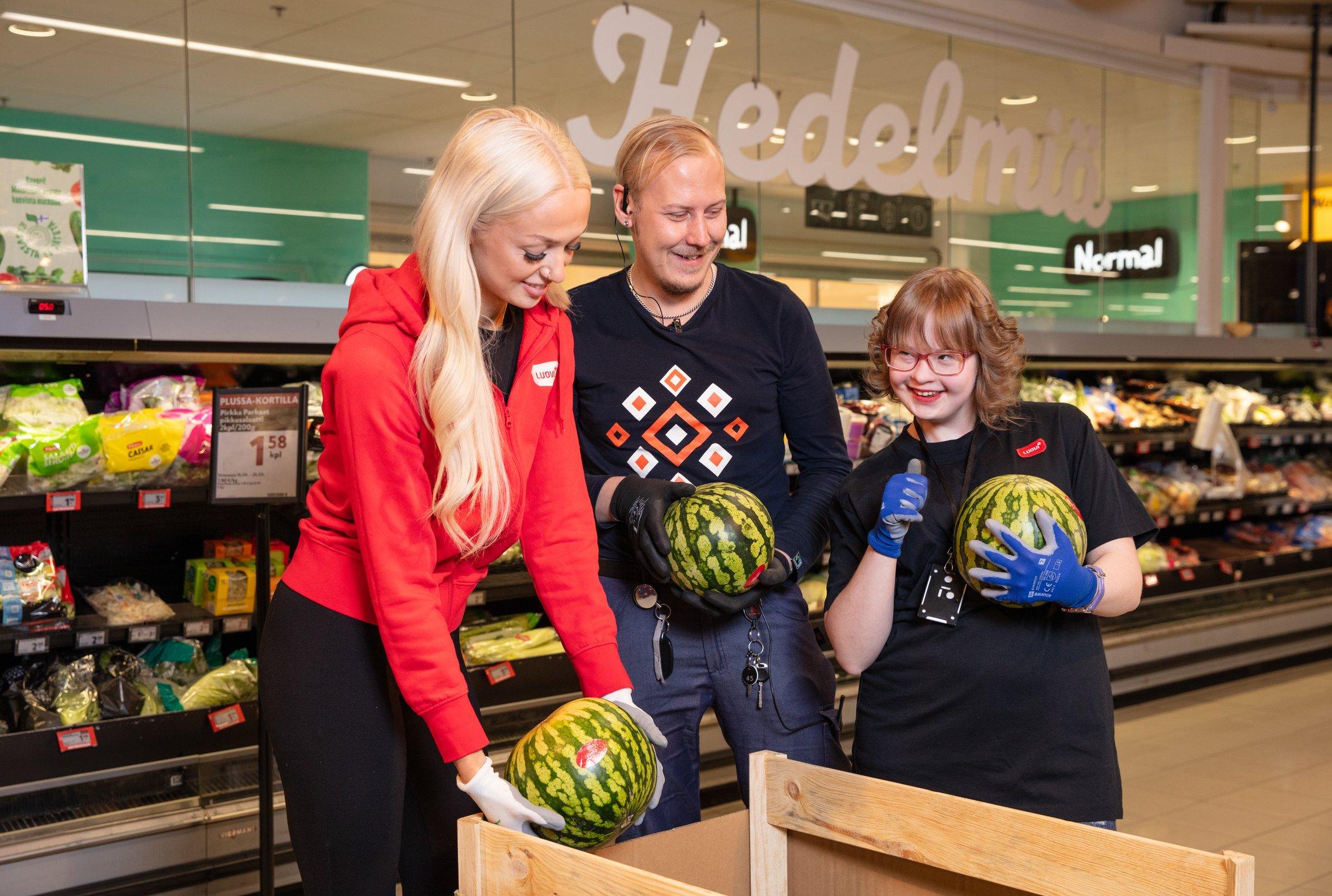Opiskelija, ohjaaja sekä kaupan työntekijä laittavat vesimeloneita näytille kaupassa.