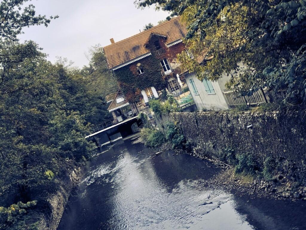 Vehreä jokimaisema, jossa vanhoja taloja ja kivimuuria.