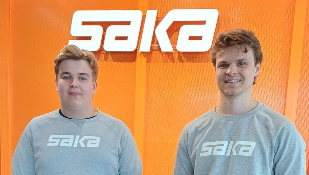 Alex ja Rasmus Nordlund päällään harmaat Saka-paidat seisovat oranssin seinän edessä, jossa on Saka-logo.